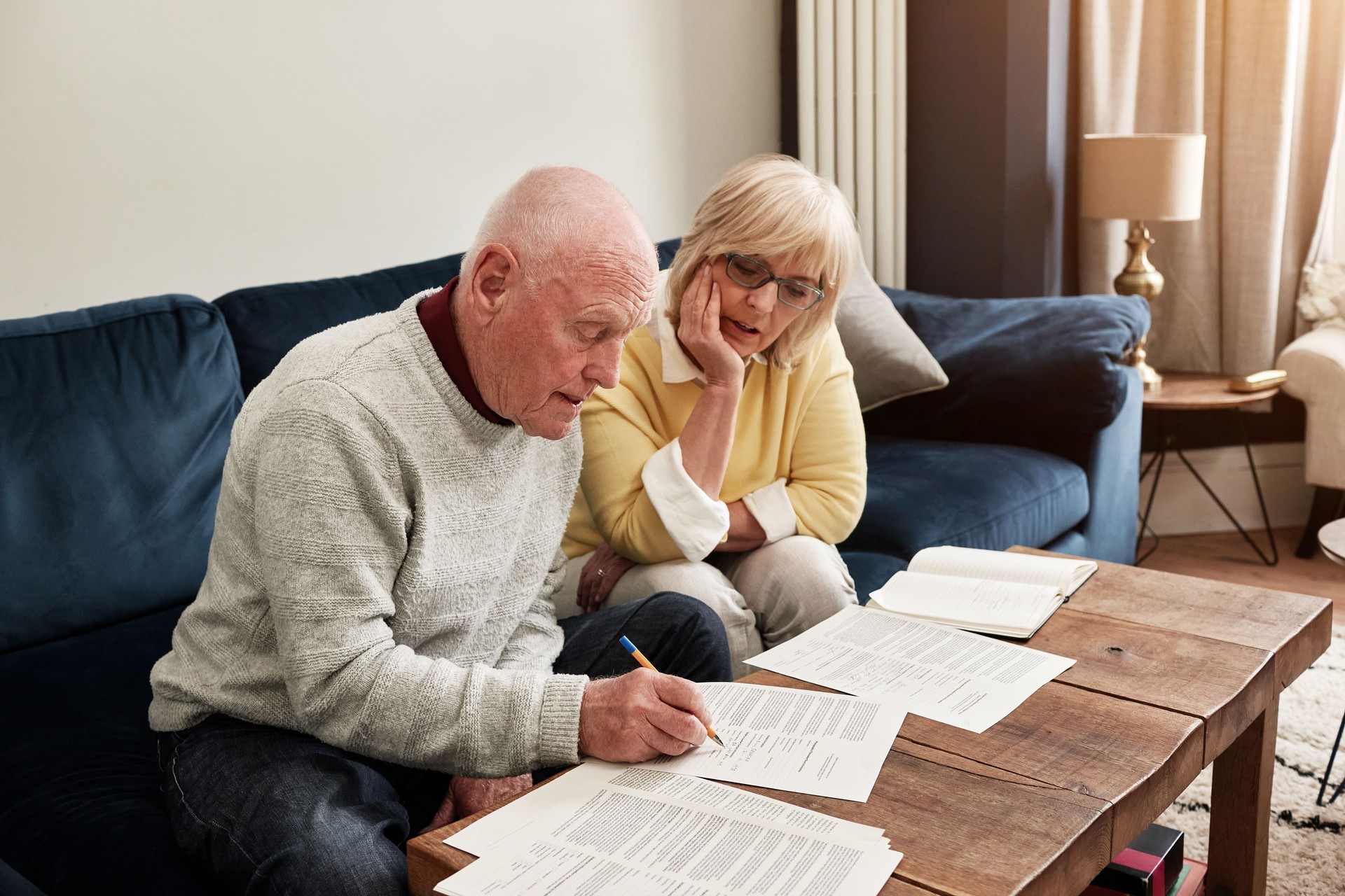 Senior, couple and writing documents in home for planning budget, retirement assets and sign legal contract for insurance policy. Man, woman and reading paperwork, finance information and investment