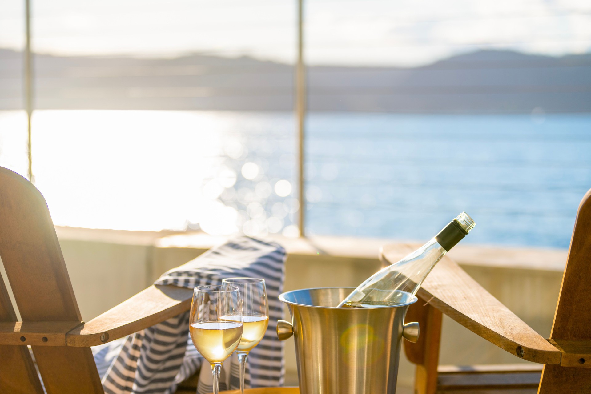 Bottle of wine with 2 full glasses beside 2 deck chairs.